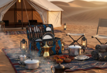 عزبة طبخ احترافية مفتوحة تعرض أدوات الطبخ المنظمة في الصحراء السعودية مع دلة قهوة عربية وخيمة في الخلفية عند غروب الشمس